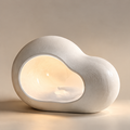 Off-white cloud-shaped table lamp with a textured rounded body and warm glowing inset on a plain background.