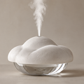 Cloud-shaped humidifier with an off-white textured top, transparent rounded base and rising mist on a plain background.