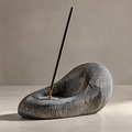 Dark textured stone incense holder with an organic curved profile, silver-tone disc and gold-tone socket on a plain background.